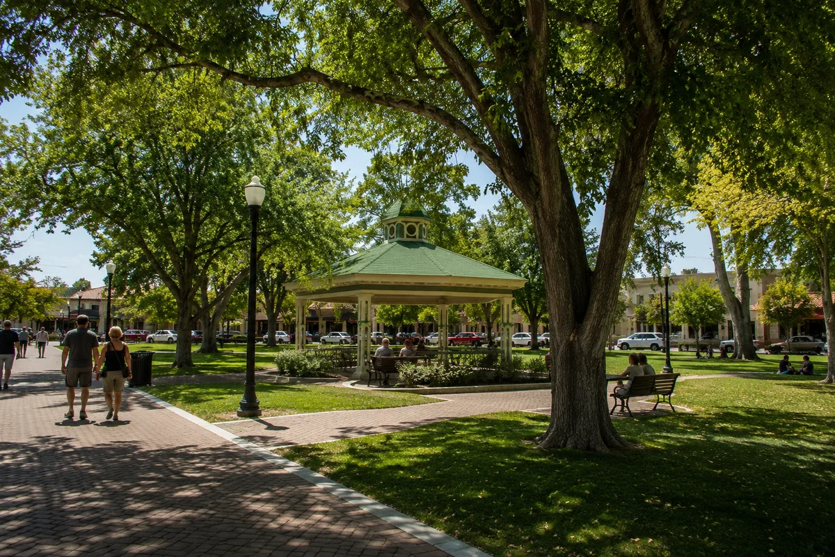 Couple walking hand-in-hand through a tree-shaded downtown park with a green gazebo in Paso Robles, a downtown worth lingering in